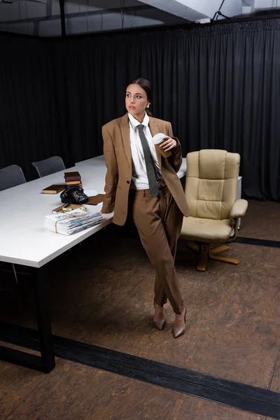 Стильная деловая женщина в костюме держит бумажную чашку, смотрит в сторону — стоковое фото
