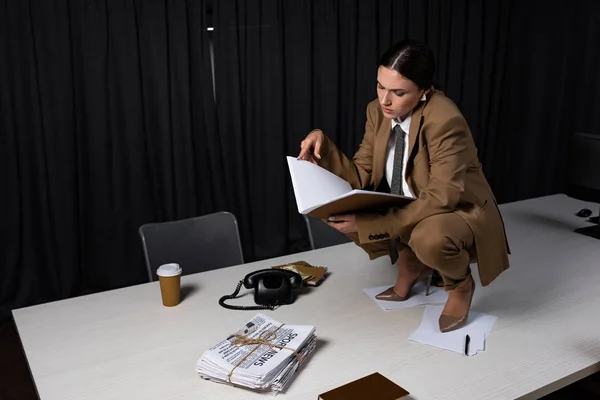 Concentrated businesswoman sitting on table, holding documents in hands — Stock Photo