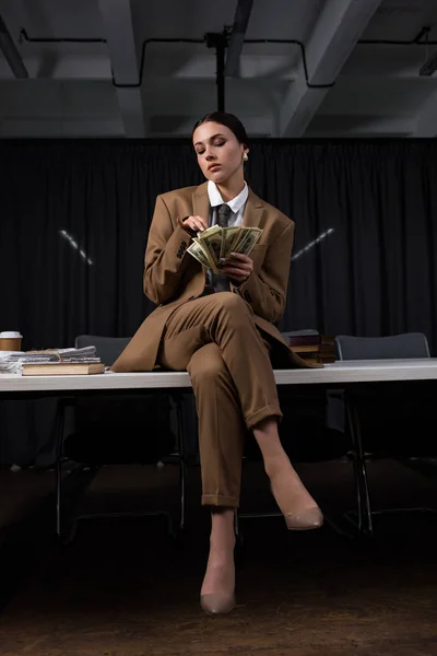 Low angle view of businesswoman sitting on table and counting money — Stock Photo