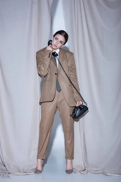 Erfolgreiche Frau im Anzug steht auf hellgrauem Vorhanghintergrund, schaut weg, telefoniert — Stockfoto