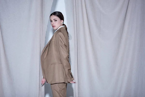 Side view of successful woman in suit standing on light grey curtain background, looking at camera — Stock Photo