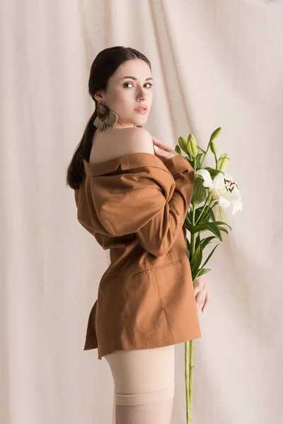 Side view of beautiful model with flowers in hands standing on curtain background, looking at camera — Stock Photo