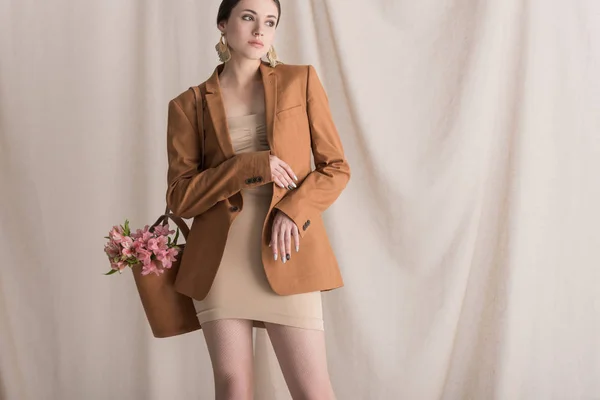 Belle femme avec des fleurs dans le sac regardant loin, debout sur le fond rideau — Photo de stock