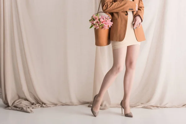 Cropped view of model in trendy wear carries flowers on shoulder bag, standing on curtain background — Stock Photo