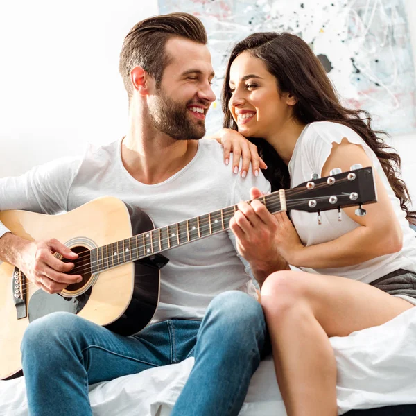 Hombre sonriente tocando la guitarra acústica mientras mira a la mujer feliz - foto de stock