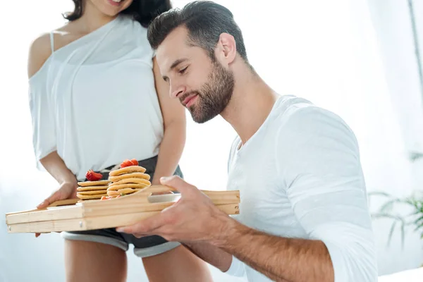 Homem bonito segurando bandeja de madeira com panquecas saborosas — Fotografia de Stock