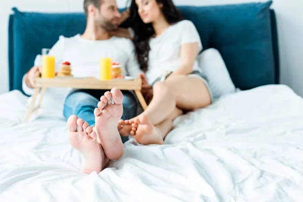 Selektiver Fokus des barfüßigen Paares, das im Bett liegt und frühstückt — Stockfoto