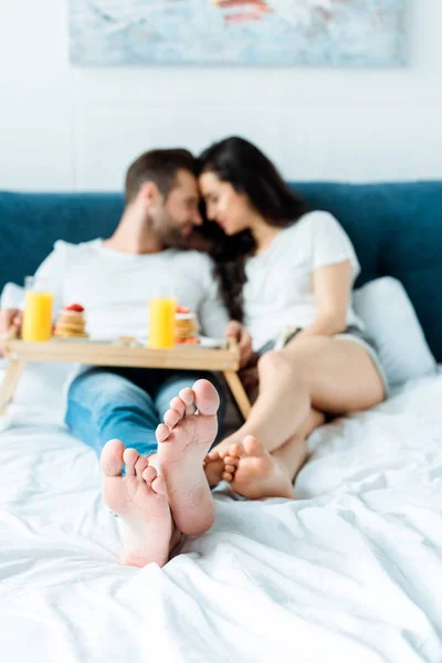 Selektiver Fokus des barfüßigen Paares, das im Bett liegt und zusammen frühstückt — Stockfoto