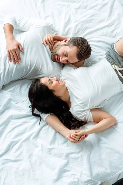 Над головой вид счастливой улыбающейся пары лежащей вместе в постели — стоковое фото