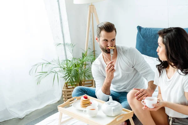 Casal engraçado sorrindo perto de bandeja de madeira com café da manhã na cama — Fotografia de Stock