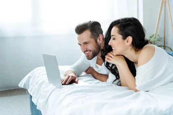 Feliz casal sorrindo usando laptop na cama juntos — Fotografia de Stock