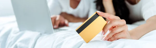 Enfoque selectivo de la mujer que sostiene la tarjeta de crédito cerca del hombre con el ordenador portátil, tiro panorámico - foto de stock