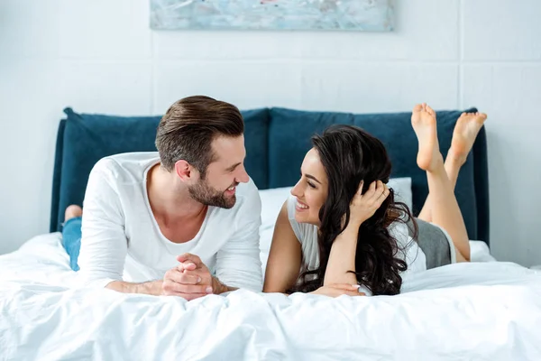 Feliz pareja acostada en la cama y mirándose - foto de stock