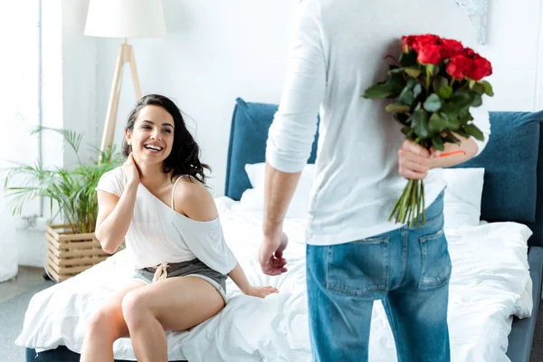 Happy woman looking at boyfriend with bouquet of red roses — Stock Photo