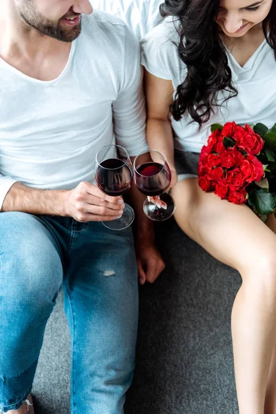 Overhead view happy couple clinking with glasses of red wine and woman holding red roses in bedroom — Stock Photo