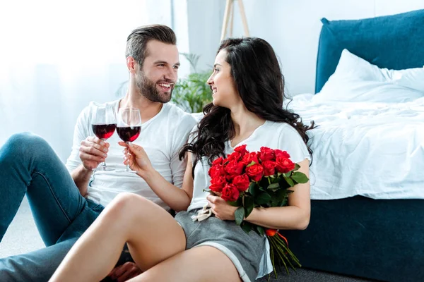 Couple cliquetis avec des verres de vin rouge et femme tenant bouquet de roses rouges — Photo de stock