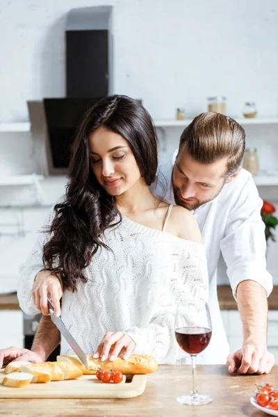 Homme regardant femme souriante couper le pain à la cuisine — Photo de stock