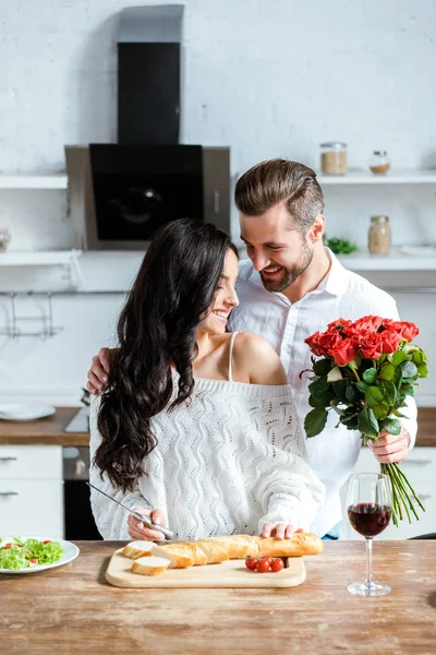 L'uomo felice che regala il mazzo di rose rosse a donna a cucina — Foto stock