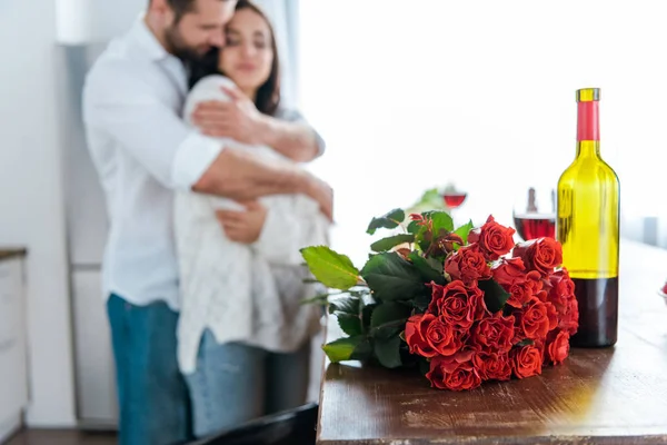 Selective focus of man embracing woman near bouquet of red roses — Stock Photo