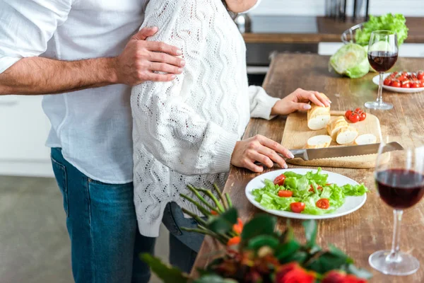 Vista ritagliata dell'uomo che abbraccia la donna vicino al tavolo con insalata e pane — Foto stock