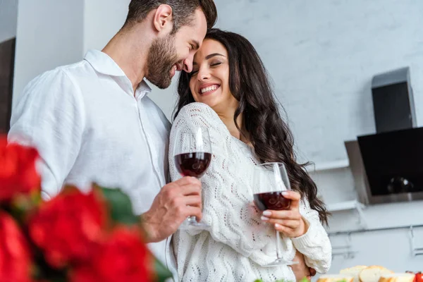 Enfoque selectivo de pareja feliz sosteniendo vasos con vino tinto y mirándose entre sí - foto de stock