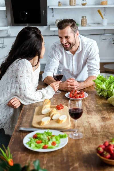 Giovane coppia che beve vino rosso al tavolo di legno con pomodorini, pane e insalata — Foto stock