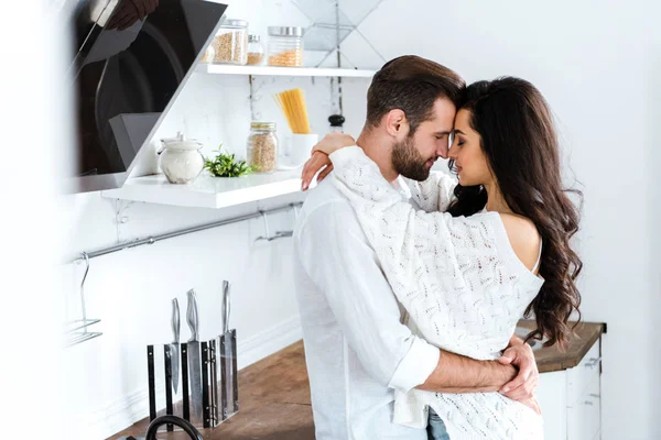 Encantadora pareja gentilmente abrazando con los ojos cerrados en la cocina - foto de stock