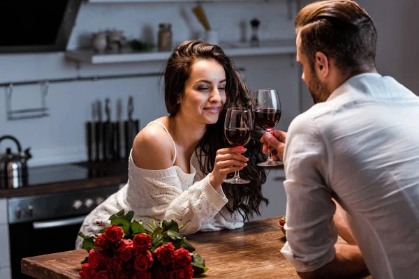 Homem e mulher clinking com copos de vinho tinto na mesa de madeira com buquê de rosas — Fotografia de Stock