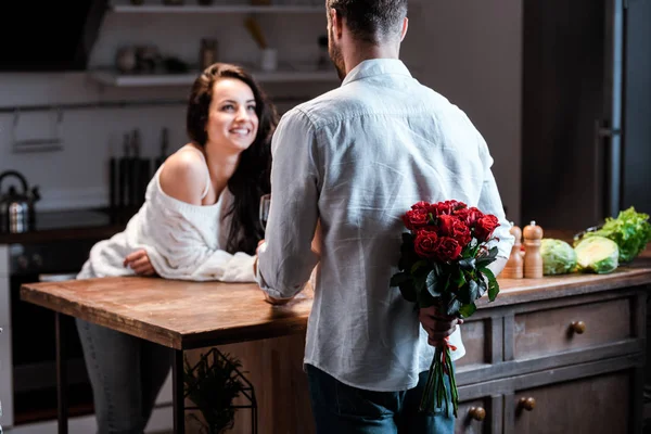 Selective focus of man holding bouquet of roses behind back and looking at smiling woman — Stock Photo