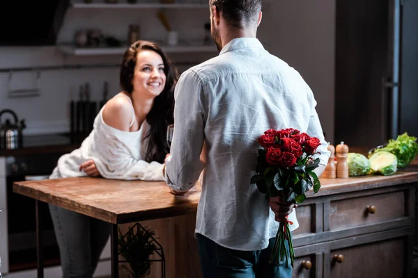 Enfoque selectivo del hombre sosteniendo ramo de rosas detrás de la espalda y mirando a la mujer sonriente - foto de stock