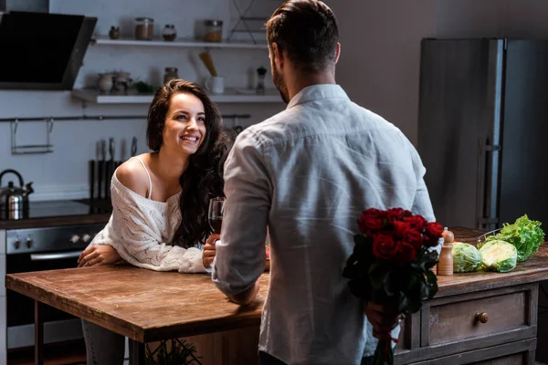 Hombre sosteniendo ramo de rosas detrás de la espalda y mirando a la mujer sonriente - foto de stock