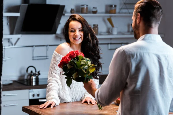 Uomo bouquet regalo di rose alla donna sorridente in cucina — Foto stock