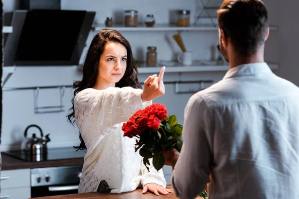Сердитая женщина показывает средний палец мужчине с букетом роз — стоковое фото