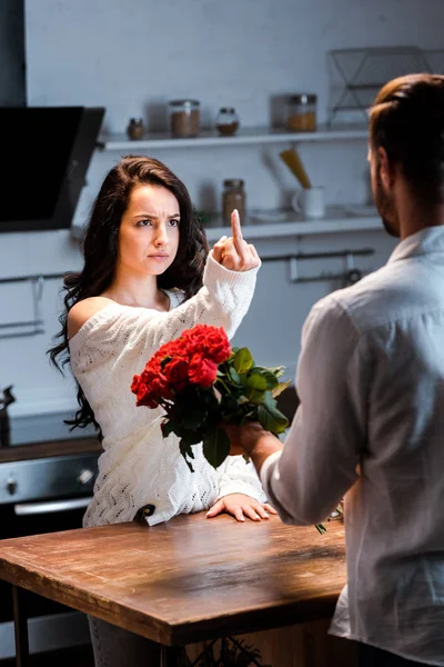 Сердитая женщина показывает средний палец мужчине с букетом красных роз — стоковое фото