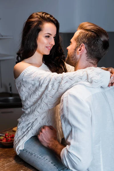 Happy woman looking at man and embracing boyfriend while sitting on table — Stock Photo