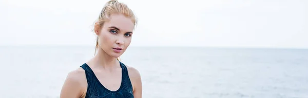 Plan panoramique de jolie jeune femme blonde regardant la caméra près de la mer — Photo de stock