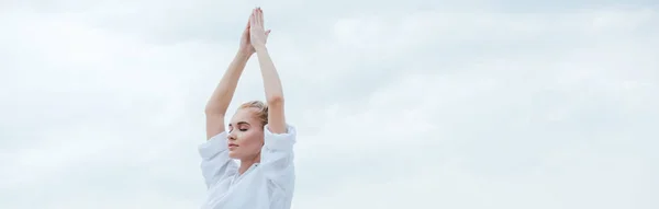 Plano panorámico de chica atractiva con los ojos cerrados practicando yoga y de pie con las manos orantes - foto de stock