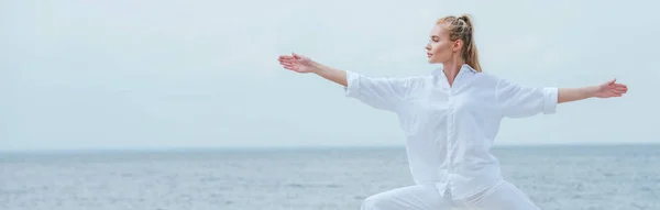 Tiro panorâmico de menina atraente praticando ioga e de pé com as mãos estendidas — Fotografia de Stock