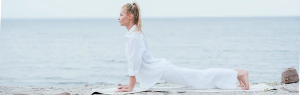 Panoramic shot of young woman practicing yoga near river — Stock Photo