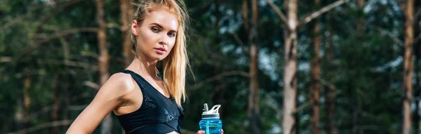 Plano panorámico de atractiva mujer deportiva sosteniendo botella de deporte - foto de stock