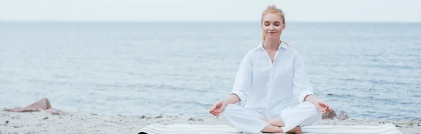 Plan panoramique de paisible jeune femme blonde aux yeux fermés pratiquant le yoga près de la rivière — Photo de stock