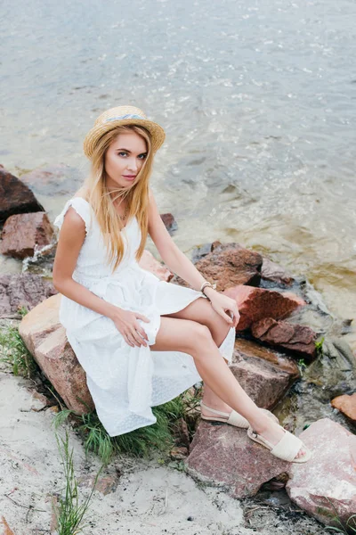 Vista aérea de mujer joven en vestido blanco sentado en piedras cerca del mar - foto de stock