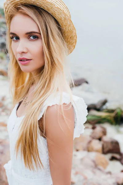 Attractive blonde woman in straw hat and white dress looking at camera — Stock Photo