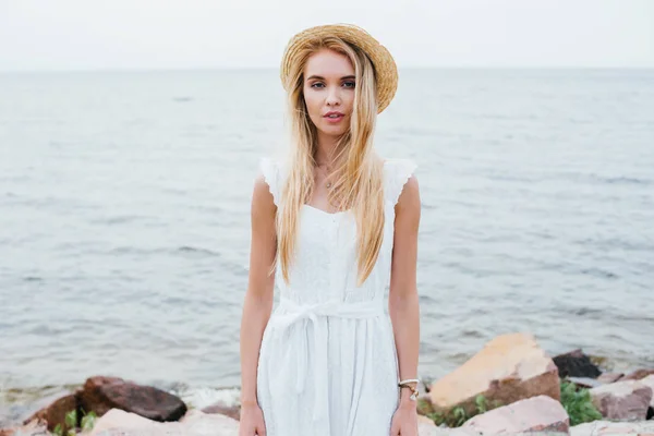 Pretty blonde girl in straw hat and while dress looking at camera — Stock Photo