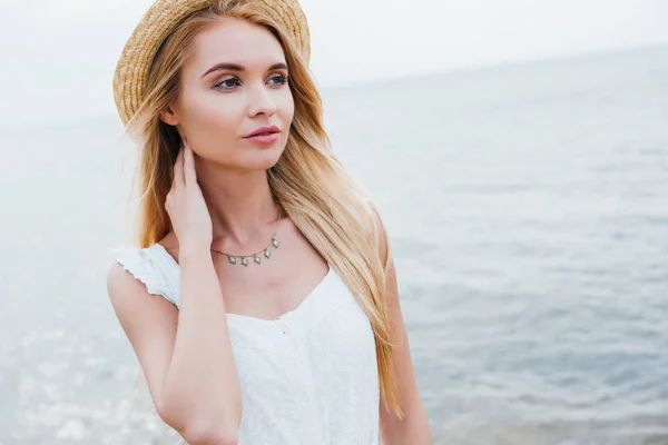 Attractive blonde young woman in straw hat touching neck — Stock Photo