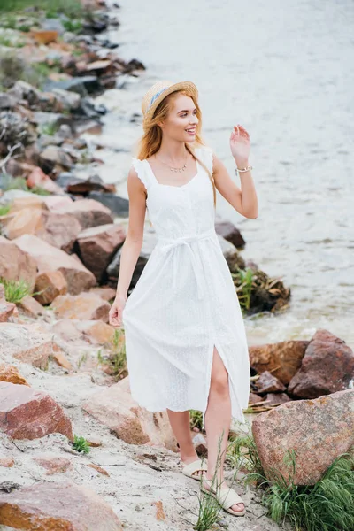 Весела молода блондинка в солом'яному капелюсі стоїть і дивиться на море — стокове фото