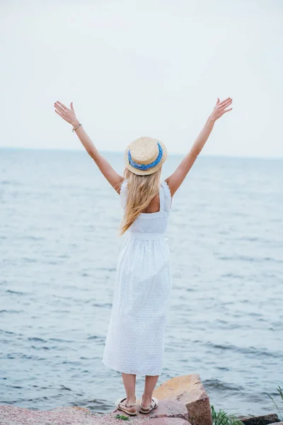 Back view of blonde woman in straw hat standing with outstretched hands — Stock Photo