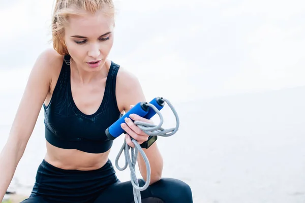 Attractive and tired young woman in sportswear looking at jump rope — Stock Photo