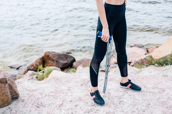 Cropped view of young sportswoman standing near sea and holding jump rope — Stock Photo