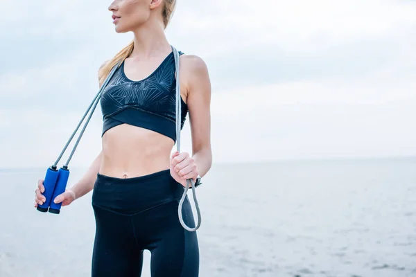 Cropped view of girl in sportswear holding skipping rope near sea — Stock Photo